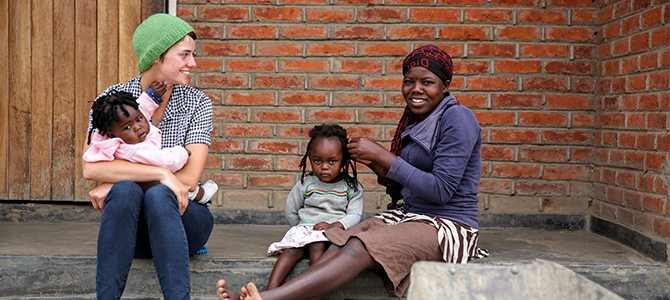 A Nu Skin employee holds a young child while she sits next to a lady braiding a young girl’s hair.